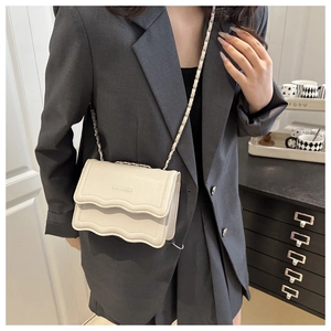 Close-up of cream crossbody bag with wavy flap design and chain strap on grey blazer
