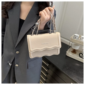 Detail of beige shoulder bag featuring a wavy flap design and elegant silver chain strap