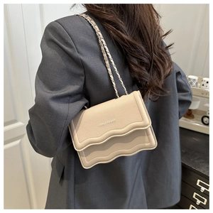 Detail view of beige pebbled leather crossbody bag with wavy flap and metal chain strap