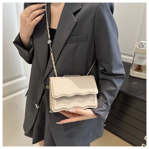 Detail of cream small square bag with scalloped edge flap and chain strap on a model