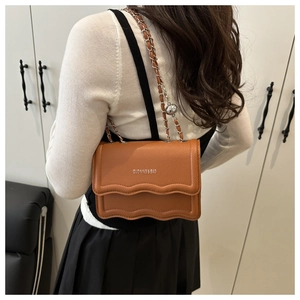 Close-up of caramel brown pebble leather crossbody bag with silver chain strap on model