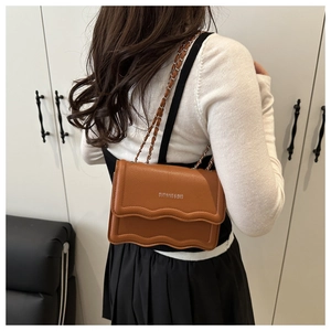 Close-up of brown scalloped leather shoulder bag with chain strap worn by a model