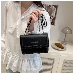 Detailed view of black litchi leather bag with wavy flap design and silver chain strap