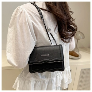 Detailed close-up of black pebble leather handbag with silver chain and wave flap design