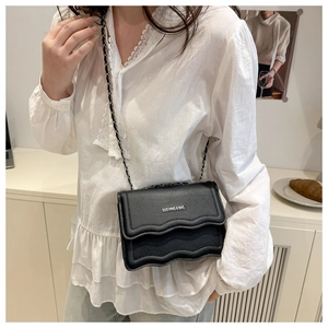 Detail of black pebbled leather crossbody bag with wave-edge flap and chain strap