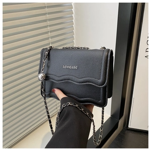Detail of black lychee grain leather crossbody bag with silver chain and metal ball charm