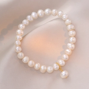 Elegant white freshwater pearl bracelet with a delicate gold pendant on silk fabric
