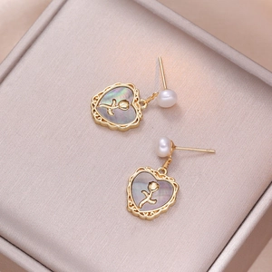 Gold heart shell earrings with rose embossing and white freshwater pearls on a jewelry display