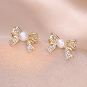 Elegant gold bow earrings with freshwater pearls and sparkling zircons on silk background