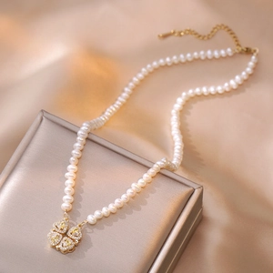 Macro-opname van parelketting met klaverhanger op champagnekleurige zijden stof
