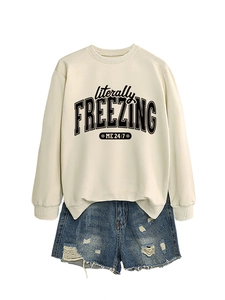 Detail of loose cream sweatshirt with literally freezing print and distressed blue denim shorts