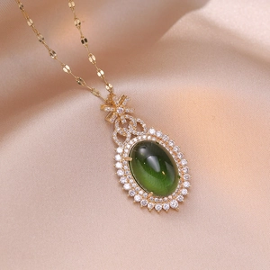 Elegant emerald zircon geometric pendant necklace with golden bow detail on silk background