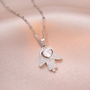 Hamsa Hand necklace with sparkling heart zircon on elegant silk background