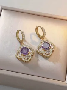 Dettaglio di orecchini a fiore dorati con zircone viola e diamanti su raso