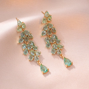 Élégantes boucles d'oreilles feuilles dorées avec gemmes vert menthe sur soie champagne