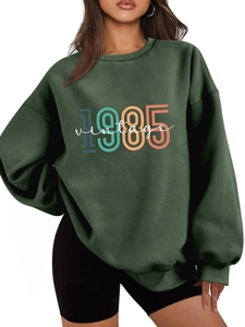 Detail of oversized dark green sweatshirt featuring a colorful 1985 vintage chest print