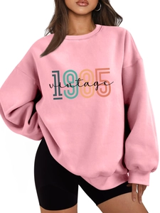 Detailed close-up of pink crewneck sweatshirt featuring a retro 1985 vintage graphic print