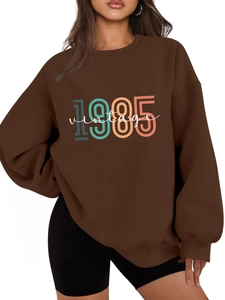 Close-up of deep brown oversized sweatshirt featuring 1985 vintage graphic print