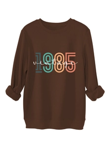 Detailed view of the 1985 vintage print on a dark brown crewneck sweatshirt ribbed cuffs
