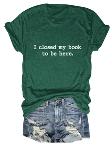 T-shirt vert foncé posé à plat avec texte imprimé 'I closed my book to be here'