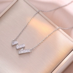 Silver wavy geometric necklace with baguette-cut zircons on a gold jewelry box