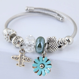 Detail of beaded bracelet featuring airplane pendant and light blue enamel daisy charm