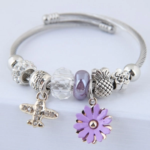 Detail view of a silver beaded bracelet with purple floral and plane pendants