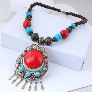 Detail of ethnic necklace featuring red gemstone pendant and metal leaf tassels