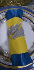 Close-up of silver glitter feather napkin ring on blue and yellow satin cloth