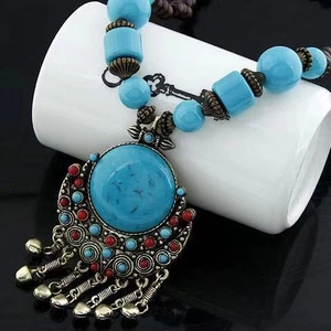 Detail of bohemian turquoise necklace with vintage bronze bells and fringe on a white stand