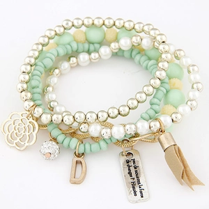 Detail of layered beaded bracelet with mint green beads, flower charms and beige tassel