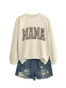 Flat lay of cream crewneck sweatshirt with MAMA camo print and ripped denim shorts