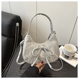 Detail of silver metallic hobo bag with bow decoration on a minimalist sofa background
