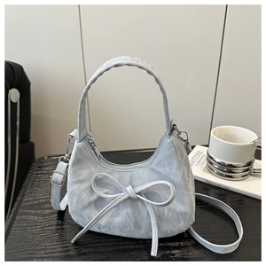 Close-up of a silver crescent hobo bag with a large bow detail on a black textured table