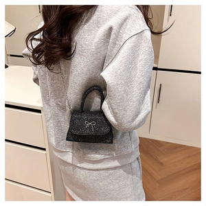 Detailed view of mini black glitter crossbody bag with elegant silver metal bow accessory