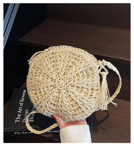 Detail of round straw shoulder bag featuring radial woven texture and chic tassel charm