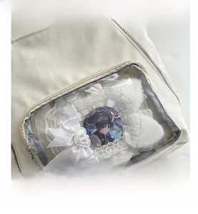 Detail of white tote bag showing transparent pocket with anime badges and lace bow