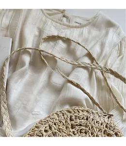 Close-up of beige woven straw shoulder bag with long strap on white pleated fabric