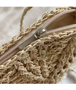 Detailed close-up of smooth metal zipper and woven texture on beige straw shoulder bag