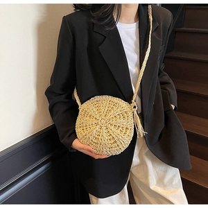 Detail of round straw bag with long tassels and woven strap on a female model