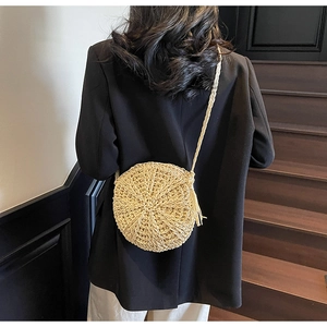 Outdoor shot of a round woven straw crossbody bag with tassels and shoulder strap details