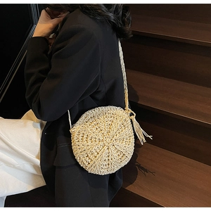Detail of round straw crossbody bag with beige woven texture and tassel charm