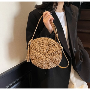 Detail of round straw shoulder bag with woven strap and long tassel fringe