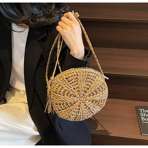 Detail of round straw shoulder bag with woven texture and tassel on a female model