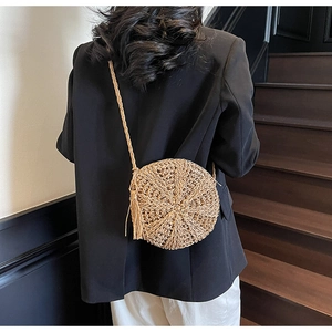 Detail of round straw shoulder bag with woven fringes and strap shown on model