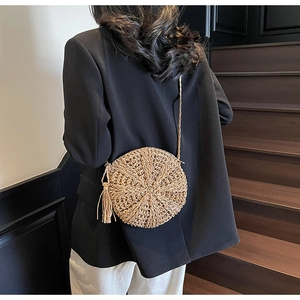 Close-up of a round straw crossbody bag with tassel detail worn by a model in a casual style