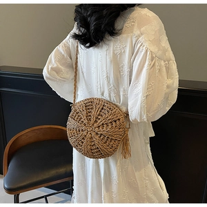 Detail of woven straw shoulder bag with long side fringe and natural woven texture