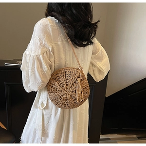 Close-up of a round straw woven shoulder bag featuring bohemian tassels and texture