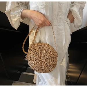 Detail of a round woven straw crossbody bag with tassels shown on a model