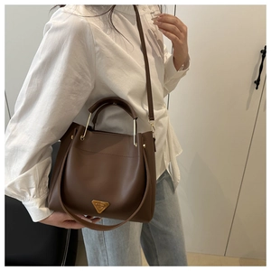 Détail du sac seau en cuir marron foncé avec une plaque triangle dorée chic